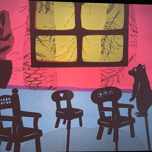 En scene fra skyggeteater. En lille bjørn ser på tre små stole. 